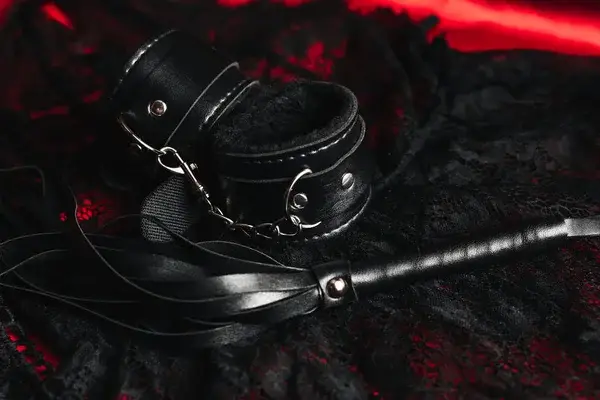 Látigo y esposas BDSM sobre sábana roja